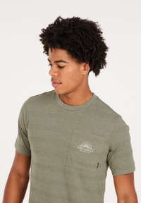 Olijfgroene t-shirt met korte mouwen van gestructureerde stof, met een borstzak en een subtiele logo-print. Ronde halslijn met een aansluitende pasvorm.