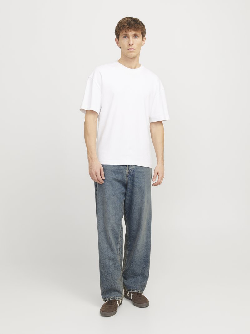 T-shirt bianca oversize, jeans in denim blu a vestibilità morbida e sneakers marroni. Design semplice con vestibilità casual e texture morbida.