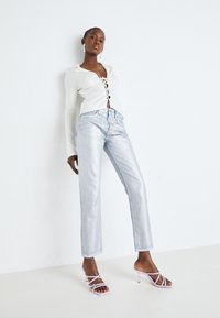 Top ligero de manga larga blanca con un frontal con cordones, combinado con jeans rectos brillantes de color azul claro. Modelo lleva tacones de tiras rosa claro.