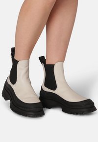 Chunky ankle boots in white leather with black elastic side panels and thick black rubber soles. Features a slight heel and pull tab.