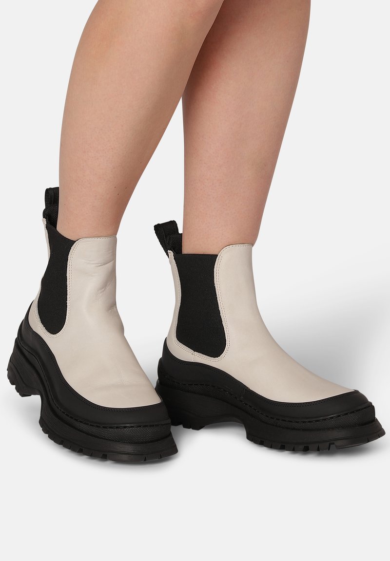 Chunky ankle boots in white leather with black elastic side panels and thick black rubber soles. Features a slight heel and pull tab.