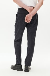 Pantaloni navy con un sottile motivo camouflage, vestibilità slim e un tessuto liscio. Abbinati a scarpe nere slip-on, visti da dietro.