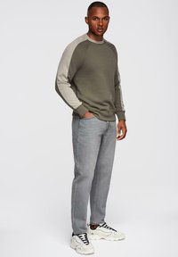 Sudadera verde oliva con mangas raglán en color beige claro, combinada con jeans gris claro y zapatillas blancas gruesas. Diseño simple y ajuste casual.