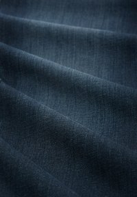 Tissu en denim d'un bleu marine profond, présentant une texture lisse avec de subtiles lignes verticales. Le tissu est plié, mettant en valeur sa flexibilité et son épaisseur.