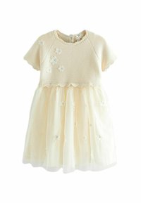 Robe couleur crème avec un corsage en tricot et une jupe en tulle transparent brodé. Présente des applications florales et un ourlet festonné. Manches courtes.