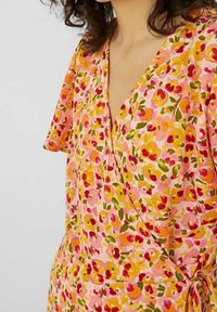 Kukkakuosisia vaatteita, joissa on vaaleanpunainen kangas ja moniväriset kukkakuviot punaisena, keltaisena ja vihreänä. Lyhyet hihat ja nauhakiinnitys vyötäröllä.