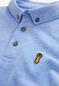 Lichtblauw polo-shirt met een gestructureerde brei. Heeft een puntige kraag, drie donkere knopen en een gele kreeft borduring op de borst.