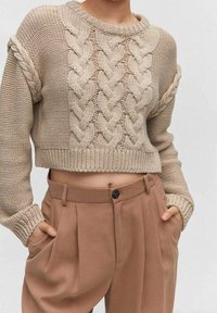 Beiger Strickpullover mit Zopfmuster, kurzem Schnitt und gerippten Bündchen, kombiniert mit hoch taillierter beiger Hose mit einem einzelnen Knopf.