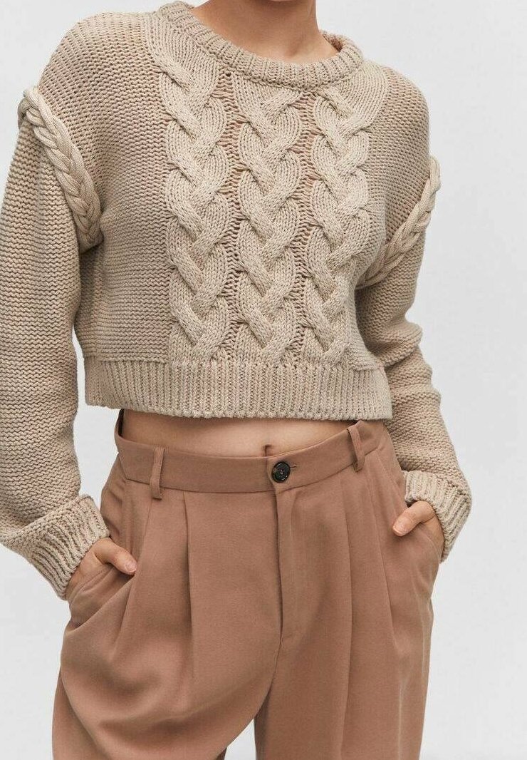 Beiger Strickpullover mit Zopfmuster, kurzem Schnitt und gerippten Bündchen, kombiniert mit hoch taillierter beiger Hose mit einem einzelnen Knopf.