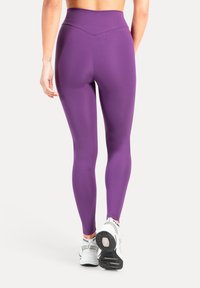 Lila högmidjade leggings gjorda av stretchigt material, med en slät yta och åtsittande design, kombinerade med vita sportskor.