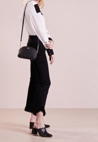 Černé džíny s vysokým pasem mají třásňový lem, doplněné bílou a černou košilí s dlouhým rukávem. Celkový vzhled dolaďuje malá černá crossbody kabelka.