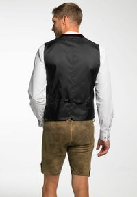 Schwarze Weste aus einem strukturierten, leichten Stoff, taillierte Passform und weinroter Kragen, kombiniert mit braunen Shorts, sichtbare Schnalle auf der Rückseite.