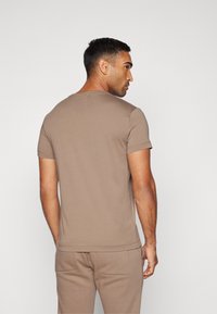 Brun kortermet t-skjorte laget av myk bomull, med rund hals og slim fit, sammen med matchende bukser med flate front.
