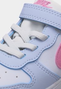 Κοντινή λήψη λευκού και ανοιχτού μπλε αθλητικού παπουτσιού με λευκά κορδόνια, ροζ λογότυπο Nike και ραμμένες λεπτομέρειες στο επάνω υλικό.