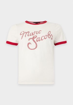 Femme debout, souriante, portant un sweat à capuche noir zippé avec de grandes poches et un pantalon noir assorti avec des détails à fermeture éclair, sur un fond uni.