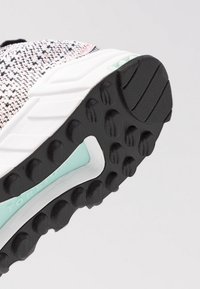 Idrottssko med texturerad svart gummisula, vit mellansula och ljus mintgrön accent. Lätt, vävd överdel med flerfärgad mönstring.