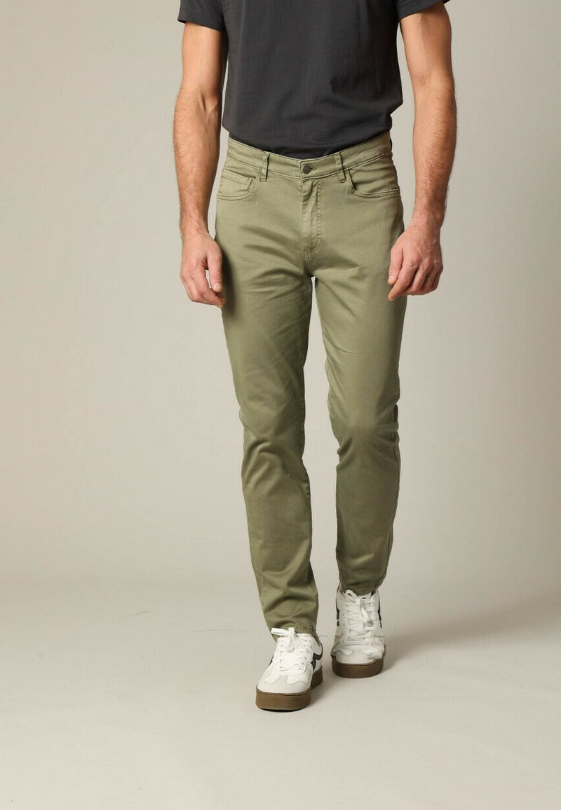 Chinos en coton vert olive avec une coupe slim, cinq poches et des détails de couture contrastants, associés à des baskets blanches et un t-shirt noir.