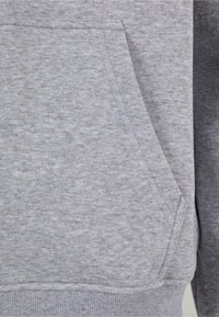 Grå sweatshirtstof med en blød tekstur, med en kengurulomme og ribbede manchetter. Glat, ensartet udseende uden mønstre.