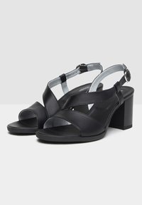 Sandali in pelle nera con cinturini incrociati, design open toe, cinturino alla caviglia regolabile e tacco chunky per una maggiore stabilità.