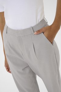 Personne portant un pantalon élégant gris clair avec des plis, la main reposant dans la poche latérale, associé à un haut à côtes blanc rentré.