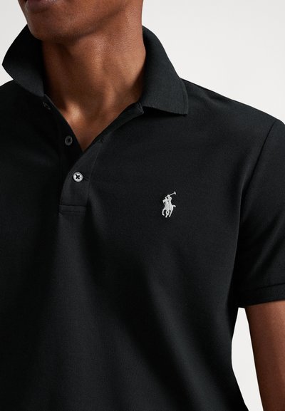 Melnas polo krekls no faktūras auduma, ar pogātu apkakli un mazu baltu izšūtu logotipu krūtīs.