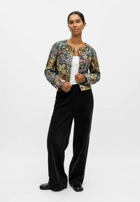 Veste matelassée à motif floral avec un col rond et des poignets côtelés, associée à un pantalon large en velours côtelé noir et des chaussures noires brillantes.
