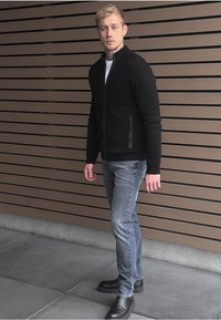 Svart zipjacka med ståkrage, i kombination med ljusblå jeans och svarta ankelskor. Slät yta och figursydd design.