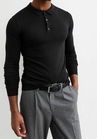 Polo noir à manches longues avec un col classique et une patte de boutonnage à trois boutons, associé à un pantalon à carreaux gris et une ceinture noire.