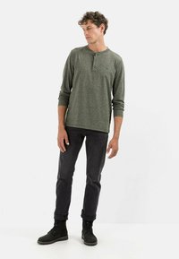 Langærmet, mørkegrøn henley skjorte med rund halsudskæring, tre-knap stolpe og tekstureret stof. Sammen med sorte jeans og snørebåndsstøvler.