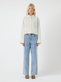 White cropped shirt with a collar, two front pockets, paired with light blue wide-leg jeans. Model wears brown suede slip-on shoes.