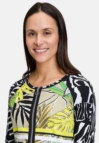 Langermige zip-up top met een mix van dieren- en tropische bladmotieven in zwart, geel, groen en beige met een geribbelde textuur.