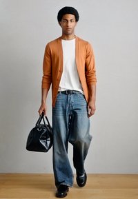 Πορτοκαλί ζακέτα, λευκό μπλουζάκι, φαρδιά μπλε τζιν, μαύρα παπούτσια και μια μαύρη τσάντα με ανάγλυφη υφή. Το μοντέλο στέκεται μπροστά σε ένα ανοιχτό φόντο.