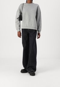 Ljusgrå sweatshirt med avslappnad passform, ribbade ärmslut och nederkant. Sparad med lösa svarta jeans och svarta platåskor. Liten svart handväska.