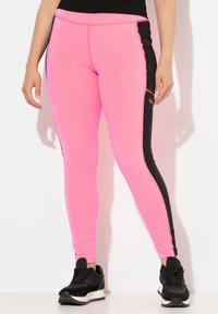 Rosa träningsleggings med svarta sidopaneler, åtsittande design och kontrasterande sömmar. Kombineras med svarta sneakers.