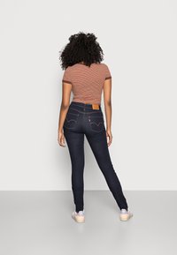 Pantalones vaqueros skinny de un azul oscuro con costuras en contraste y un parche de cuero en la cintura. Combinados con una camiseta de rayas de manga corta y zapatillas.
