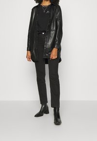 Black leather button-up shirt jacket over a black t-shirt, paired with black straight-leg jeans and ankle boots.