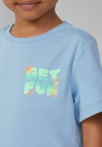 Lichtblauw katoenen T-shirt met korte mouwen en een ronde halslijn. Voorzien van neon groene tekst "GET FUN" en graphics van de zon en een surfplank.