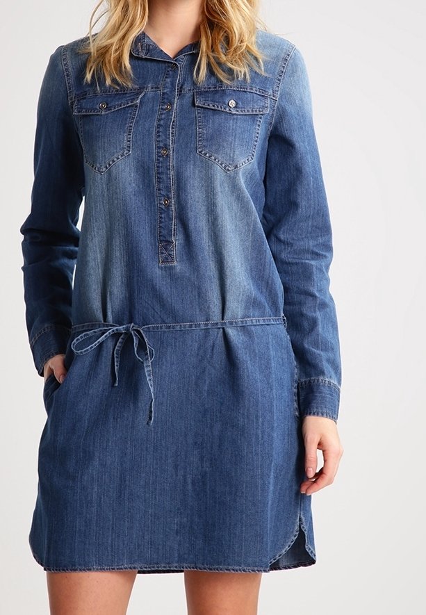 Denimmekko, jossa on pitkät hihat, napitus edessä, kaksi rintataskua, nyöri-vyötärö ja hieman kaareva helma eri sävyissä sinistä.