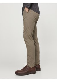 Pantalon chino kaki à coupe slim, poches avant et texture de tissu lisse, associé à des chaussures marron à lacets avec une semelle robuste.