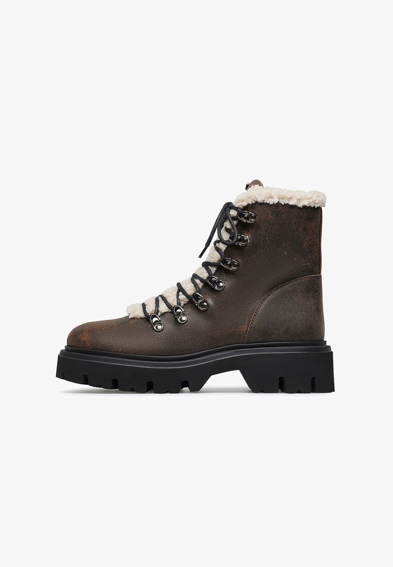 Stivaletto in pelle marrone con lacci, suola nera spessa e rivestimento in pile bianco visibile sulla caviglia e sulla linguetta.
