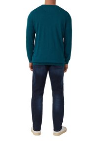 Türkiser Pullover aus weichem Strick, mit langen Ärmeln und rundem Halsausschnitt, kombiniert mit dunkelblauen Jeans und weißen Sneakers.