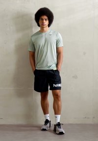 Maglietta sportiva a maniche corte verde chiaro, pantaloni corti neri con logo "NIKE" e scarpe da corsa grigie. Tessuto liscio, design semplice.