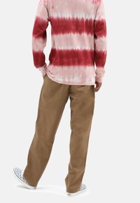 Chemise à manches longues tie-dye rose et rouge, associée à un pantalon beige et des chaussures slip-on à damier, vue de dos.