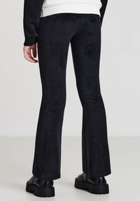 Pantaloni a zampa d'elefante in corduroy nero con una texture a coste, vita alta e una leggera lucentezza, abbinati a stivali neri chunky.