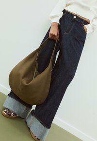 Maslina zelena torba hobo s patentnim zatvaračem, u kombinaciji s visokim tamnim farmerkama širokih nogavica i kontrastnim svijetlim denimski manžetama.