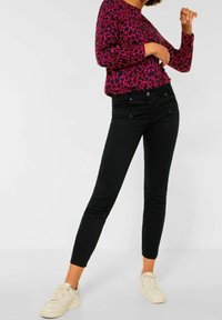 Fuchsia Langarmshirt mit Leopardenmuster, kombiniert mit schwarzen, eng anliegenden Jeans und weißen Sneakers, mit Fronttaschen und schlankem Design.