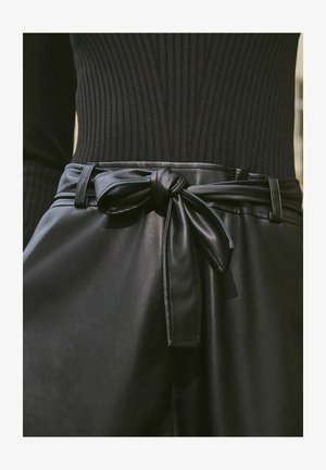 Mustmust mustrid kleidid, millel on sile tekstuur, ja vöökoht on seotud vööga, ning selle peal on must triibuline top.