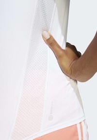 Vit idrottströja med nätpanel på sidan och sömdetaljer, tillsammans med ljusrosa byxor med vita ränder. Ytan verkar sl ät.