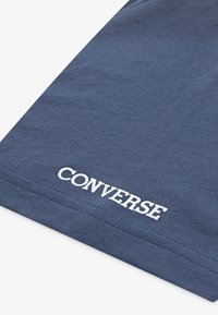 Kraljevo modra bombažna majica s belim logotipom "CONVERSE" na robu, gladka tekstura in standardni kroj.