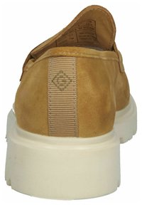 Tan suede slip-on shoe with a textured back, featuring a vertical fabric stripe and a white rubber sole. Label visible inside the shoe.
